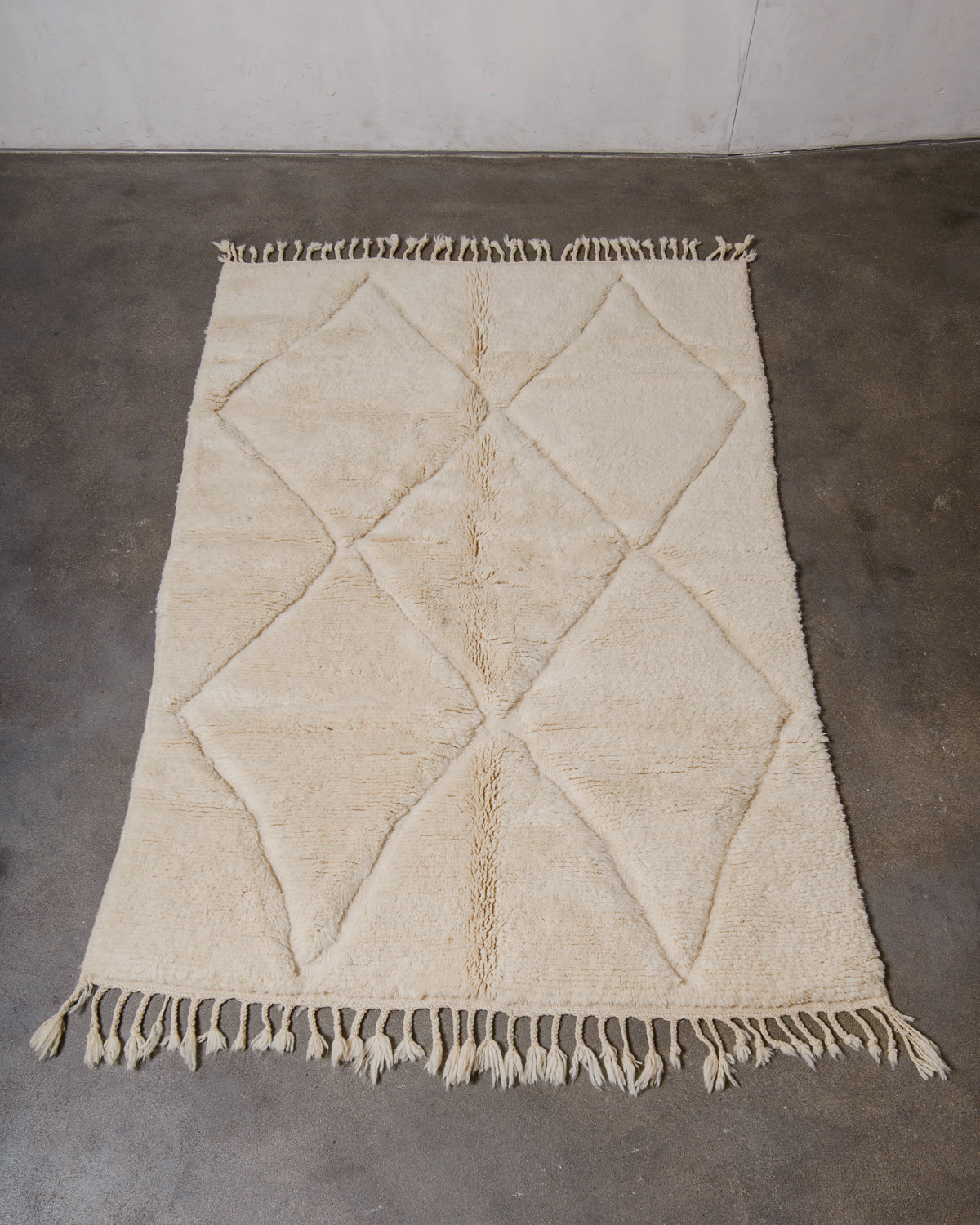Beige diamond patterned rug with fringe on a concrete floor